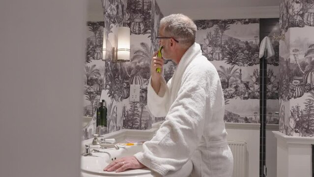 Man wearing dressing gown finishes a dry shave in a bathroom, locked off