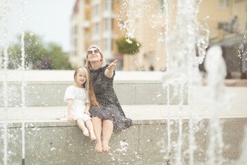 Young pretty mother and her daughter having fun together near the fountain. Cheerful family having fun.