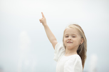 Look there. Smiling little girl on the sky background pointing up with her finger. Focus at her...