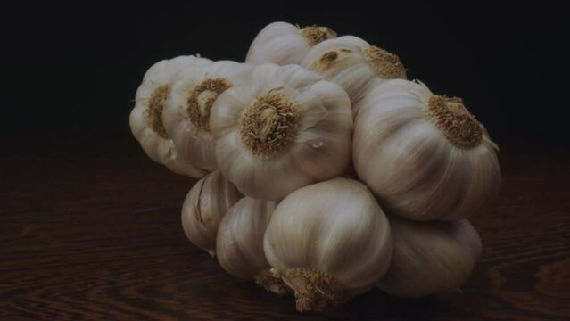 Dolly out view of aesthetically pleasing braided garlic cloves on a textured wooden table. Close-up shot.