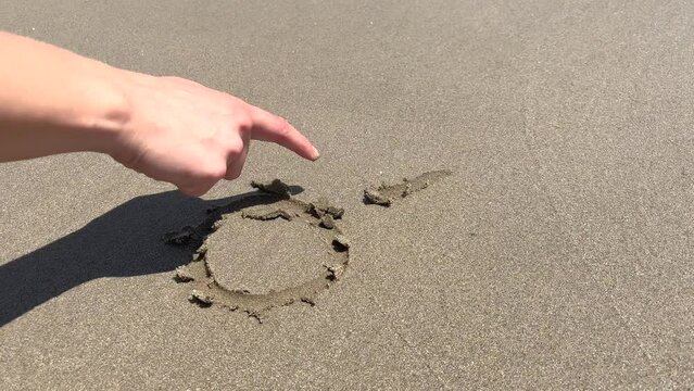 woman's hand drawing a sun in the wet sand of the beach