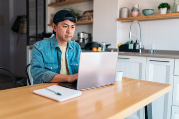 Asian man working with a laptop from the kitchen