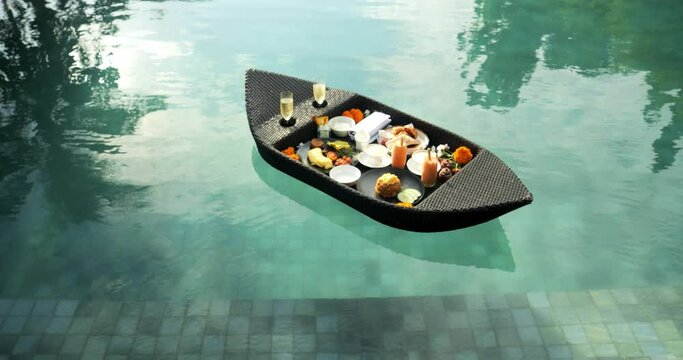 Slow motion shot of a floating breakfast in bali with healthy breakfast with coffee, bread and smoothies with champagne by the side in a pool during a nice trip