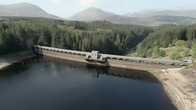 Aerial view of Laggan Dam on a sunny day on the River Spean, Loch Laggan, Scottish Highlands, Scotland, UK. Rotating right to left around the loch side of the dam.