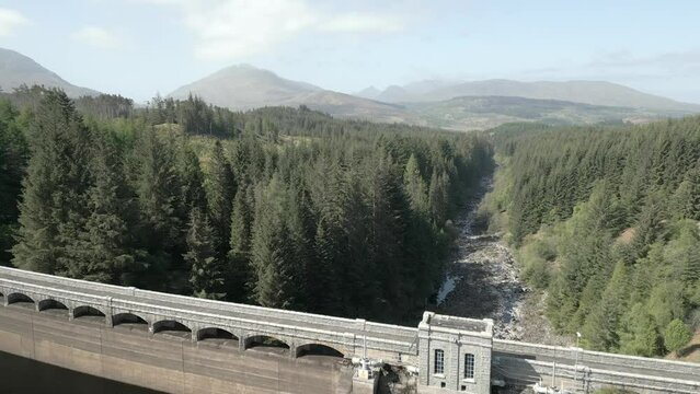 Aerial view of Laggan Dam on a sunny day on the River Spean, Loch Laggan, Scottish Highlands, Scotland, UK. Flying in reverse over the top of the dam from the river side.