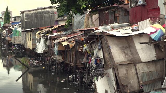 Crudely build houses next to a river in a slum area in Manilla. Trash floating about in the river.