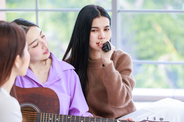 Closeup shot of Millennial two Asian beautiful cheerful female LGBTQ lover couple girlfriends in casual outfit sitting cuddling embracing smiling holding playing guitar singing songs music together - Powered by Adobe
