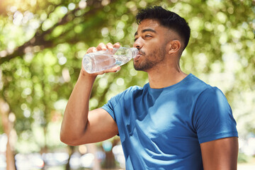 Fitness, man or runner drinking water outdoor for exercise, training or running at a park. Indian male athlete in nature for a workout, run and break to drink from a bottle for health and wellness