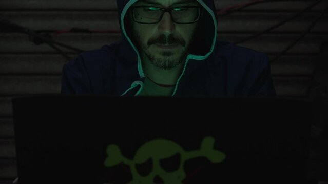 Computer hacker with his laptop works to introduce viruses into the network from a dark room, Hacker from a hideout
