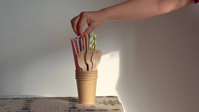 A person's hand takes a biodegradable cardboard straw from a glass with more sustainable objects. overall picture

