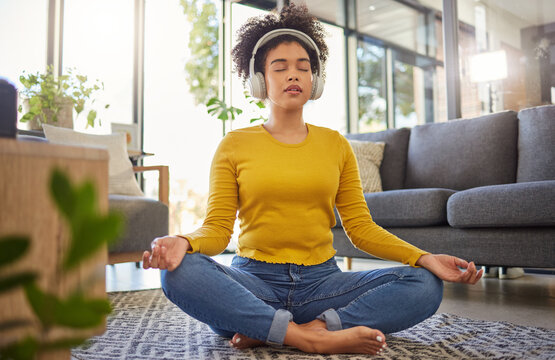 Meditation, headphones and woman in home wellness, mental health or yoga podcast in living room. Music, streaming and african person meditate, holistic exercise and peace or lotus on audio technology