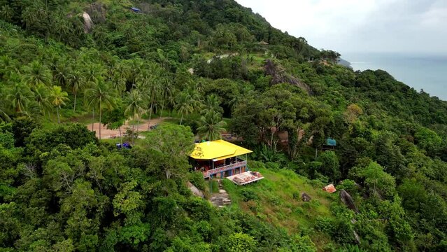 Drone shot of Tomorrowland cafe, wow viewpoint party location. Techno festival on Koh Phangan in Thailand. House on hilltop surrounded by palm trees and jungle. pick up Trucks in front of the house.