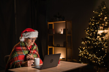 Santa Claus is watching a movie online using a laptop, sitting at the table wrapped in a checkered...