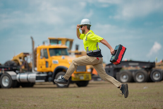 Hispanic 40 s builder excited jump on site construction. Excited builder construction worker in a safety helmet jumping in front of the trucks. Excited crazy builder man in helmet jump outdoor.