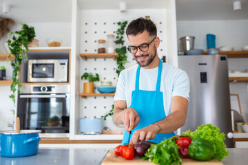Fototapeta na wymiar Handsome young man man stand at modern kitchen chop vegetables prepare fresh vegetable salad for dinner or lunch, young male cooking at home make breakfast follow healthy diet, vegetarian concept