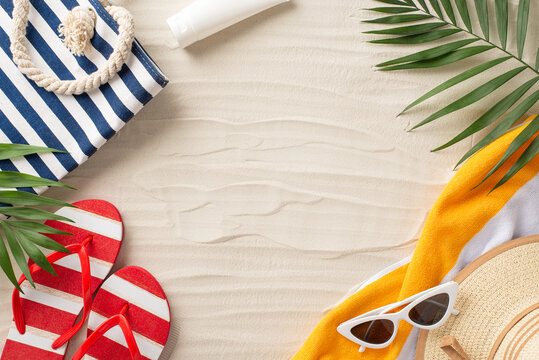 Vacation essentials laid out on sandy beach background: top view sunglasses, sunhat, beach bag, flip-flops, sunscreen bottle, towel, palm leaves. Perfect for a summer getaway!