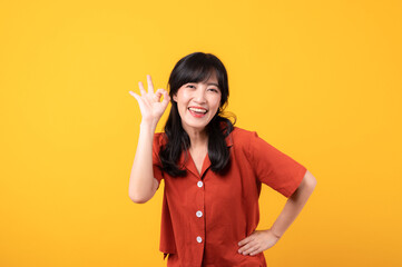 Portrait young beautiful asian woman happy smile dressed in orange clothes looking surprised, reacting amazed, raising eyebrows impressed isolated on yellow studio background.