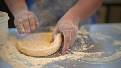Close up of a chef cook hands and fingers pushing and pressing dough, flipping and turning it and giving round form to it