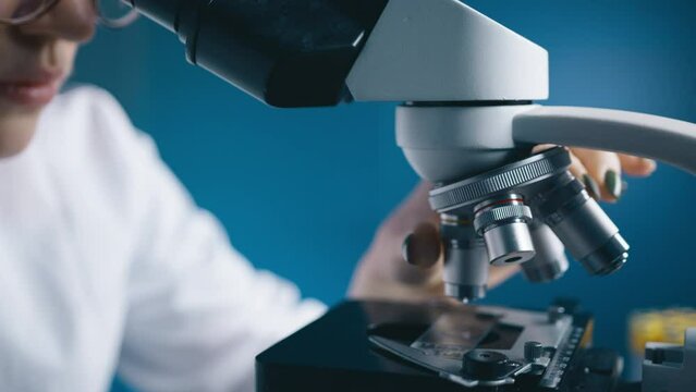 Female studying DNA mutations by looking and rotating microscope in modern medical science laboratory. Microbiologist working with microscope analyzing samples. Scientist working High-Tech Equipment
