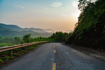 Landscape photo of mountain pass road with trees and valleys, village fields below at dawn.
