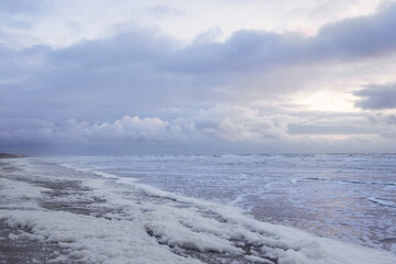 Sea foam along the surf line on the sandy shore of the North Sea at sunset on a windy evening