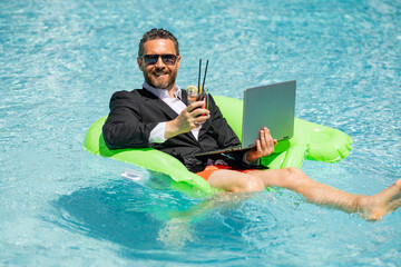 Crazy summer. Business drink summer cocktail and using laptop in suit in water pool. Fun business...