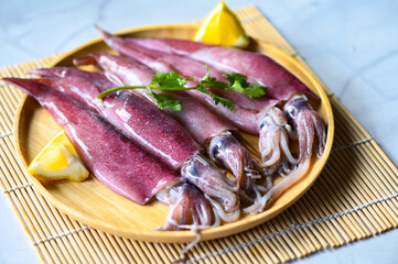 fresh squids octopus or cuttlefish for cooked food at restaurant or seafood market, Raw squid on plate with salad spices lemon on wooden background
