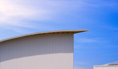 Side view of corrugated iron wall with curve shed roof of modern warehouse building against blue...