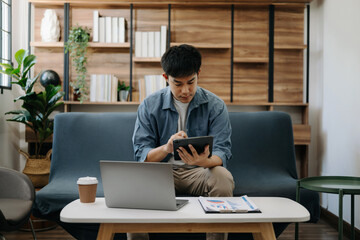 Fototapeta premium Young business man working at office with laptop, tablet and taking notes on the paper. on sofa in liveing room at home..