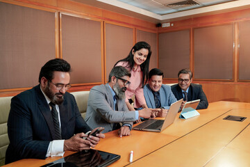 Young indian woman presenting project information to other businesspeople, using laptop at meeting hall