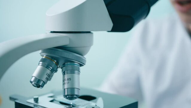 Close up microbiologist in white medical uniform looks under microscope analyzing sample. Smart scientist working with High Tech Equipment. Slow motion bright innovative science laboratory 4K