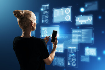 Attractive blonde woman using cellphone with glowing business chart holograms on blurry blue background. Finance, growth and company report concept.