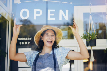 Portrait, nursery and open with a woman hanging a sign in the window of her shop for gardening. Small business, garden center and an excited young female entrepreneur opening her new flower store