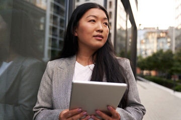 Business Chinese woman standing next to the building and holding digital tablet