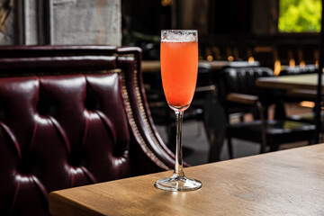 Rossini cocktail made of strawberry puree, lemon juice and prosecco sparkling wine served in a flute glass, on a wooden table in a restaurant or bar, horizontal photo