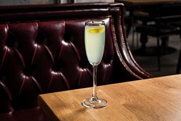 French 75 cocktail made of gin, lemon juice, sugar simple syrup, prosecco sparkling wine served in a flute glass garnished with lemon twist, on a wooden table in restaurant or bar, horizontal photo