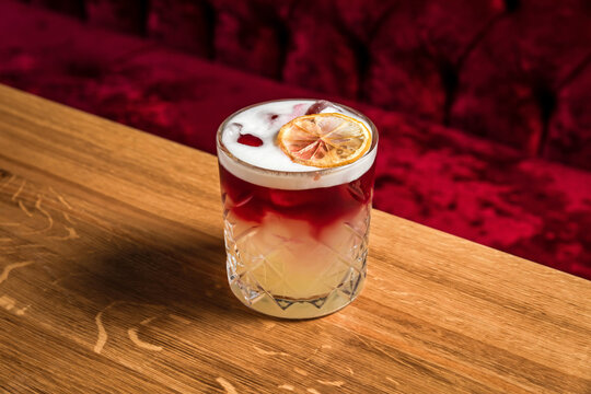 New York sour or Continental sour cocktail with bourbon or whisky garnished with dried lemon wheel at the wooden table at bar or restaurant, horizontal photo