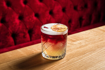 New York sour or Continental sour cocktail with bourbon or whisky garnished with dried lemon wheel at the wooden table at bar or restaurant, horizontal photo