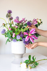 Vase with fresh summer flowers in female hands on a white background.