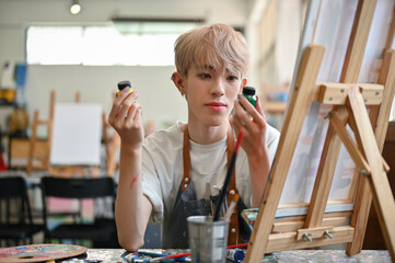 A creative Asian gay male artist chooses watercolors for his creative painting on a canvas