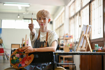 A professional Asian gay man artist sits on a chair in his creative studio