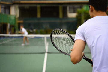 Back view of tennis player standing in ready position to receive a serve, practicing for competition on a court