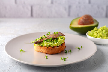 Sandwiches with sprats on toasted slices of bread. Sandwich with smoked sprat - fish, avocado and microgreens.