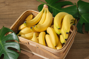 Bananas are arranged inside a bamboo basket decorated with some fresh green leaves. Banana...