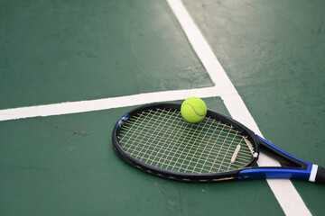 A tennis racket and ball on green floor of the court with sunlight. Outdoor sports and healthy lifestyle concept