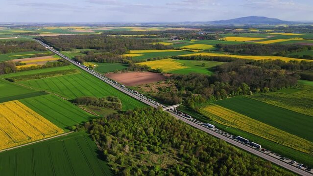 Traffic jam on highway near colorful agriculture fields. Blooming rapeseed fields and green meadows, aerial view