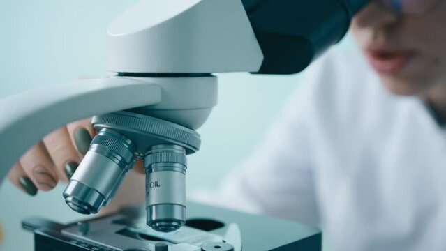 Smart scientist working with High Tech Equipment. Slow motion bright innovative science laboratory 4K. Close up microbiologist in white medical uniform looks under microscope analyzing sample