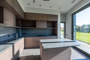 Empty kitchen with a marble table in the center, wooden cabinets in a modern minimalist style and a large panoramic window