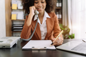 Business woman involved in cellphone call conversation working on computer and documents, giving professional consultation to client or negotiating project successful.