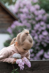 Spring flowering. Portrait of a beautiful little girl 3 years old with lilac flowers in nature....
